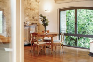 A dining area with a round wooden table, four chairs, a vase with flowers, and a stone wall.