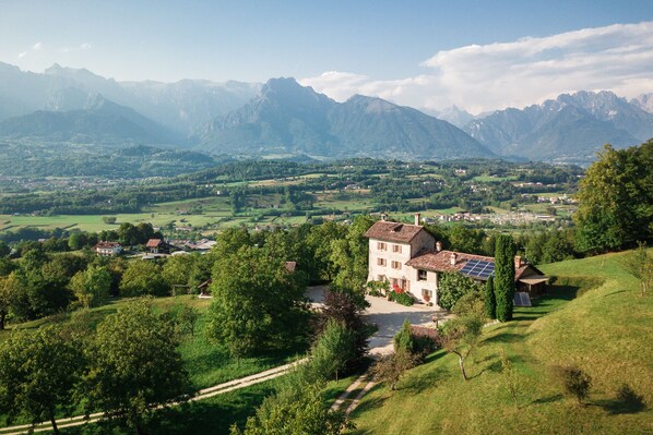 A rural house with a solar panel, surrounded by lush greenery and mountains in the background.