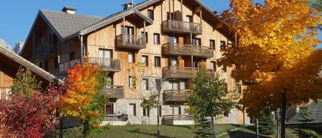 A multi-story wooden building with balconies, surrounded by autumn foliage.