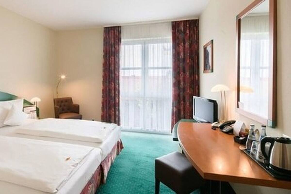Habitación de hotel con dos camas, un escritorio con teléfono, televisor y una ventana con cortinas.