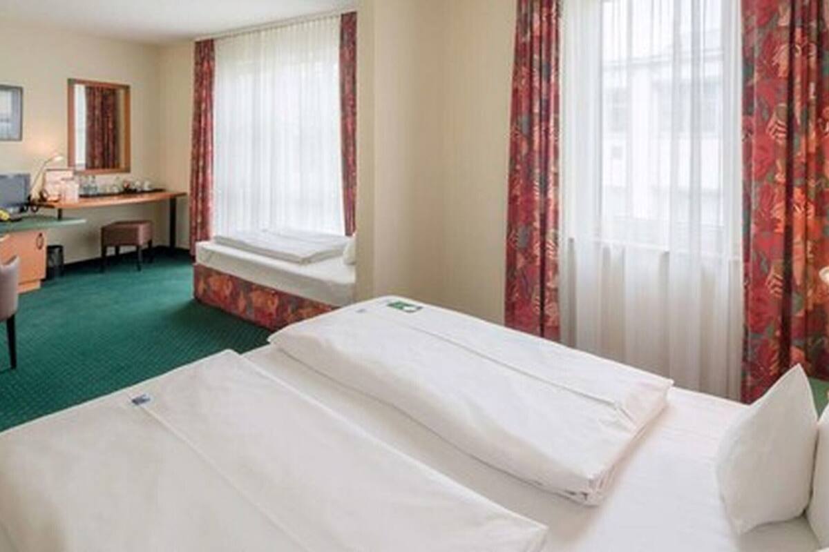 Habitación de hotel con dos camas individuales, un escritorio, una silla y una ventana con cortinas.