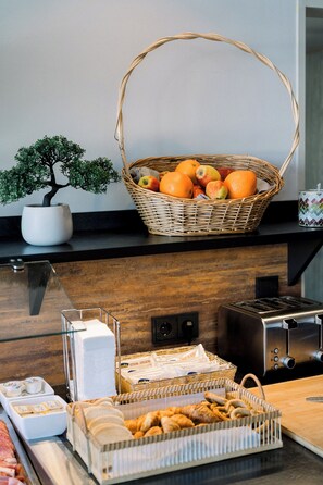 A kitchen counter with a fruit basket, a potted plant, and various food items. - Highway Hotel Dasing – Augsburg (Dasing)