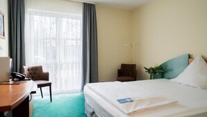 Een hotelkamer met een bed, bureau, stoel en een raam met gordijnen.