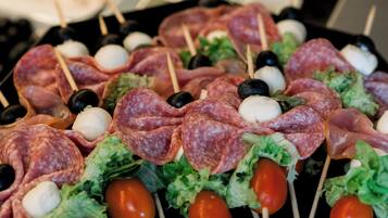 Eine Auswahl an Speisen, darunter Spieße mit Fleisch, Oliven und Cocktailtomaten, auf einem Tablett angerichtet.