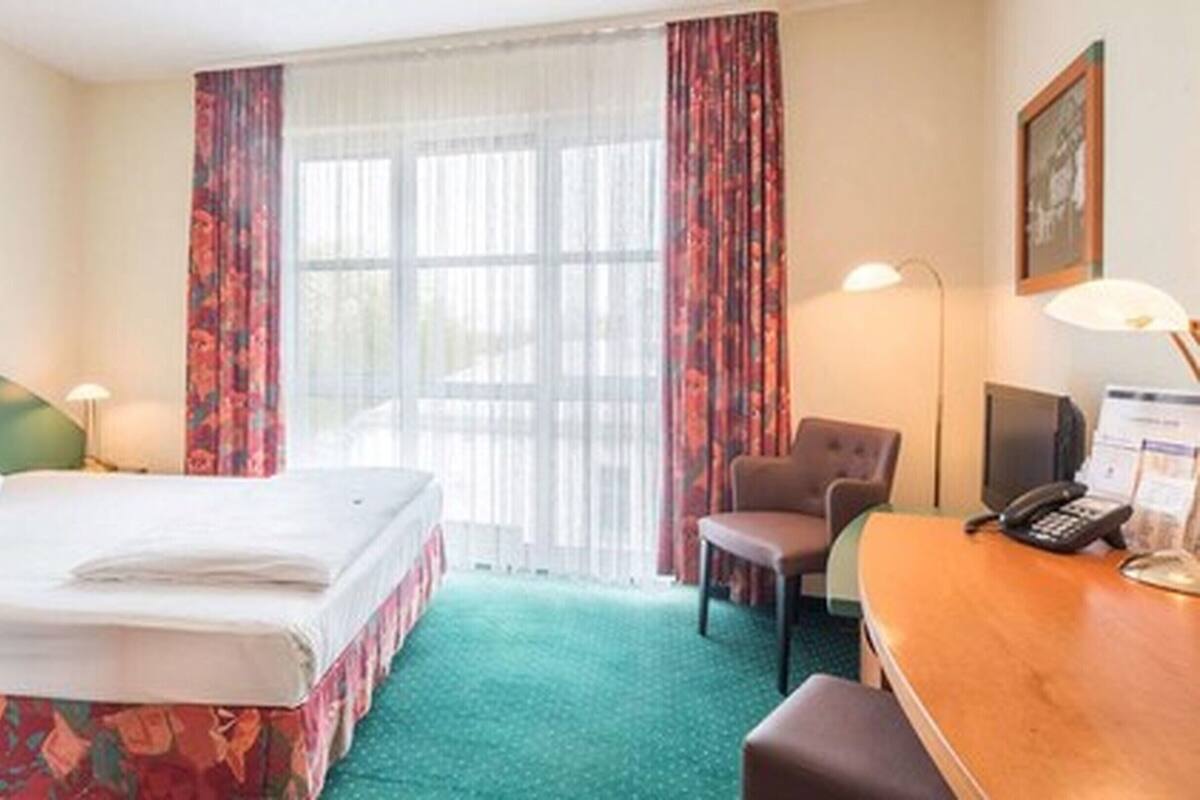 Una habitación de hotel con una cama, un escritorio con teléfono, una silla y una lámpara.