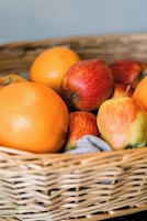 Una cesta de mimbre con manzanas y naranjas.