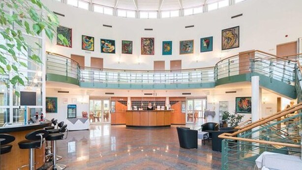 Een ruime lobby met een centraal gelegen bar, meerdere niveaus met glazen balustrades en kunstwerken aan de wanden.