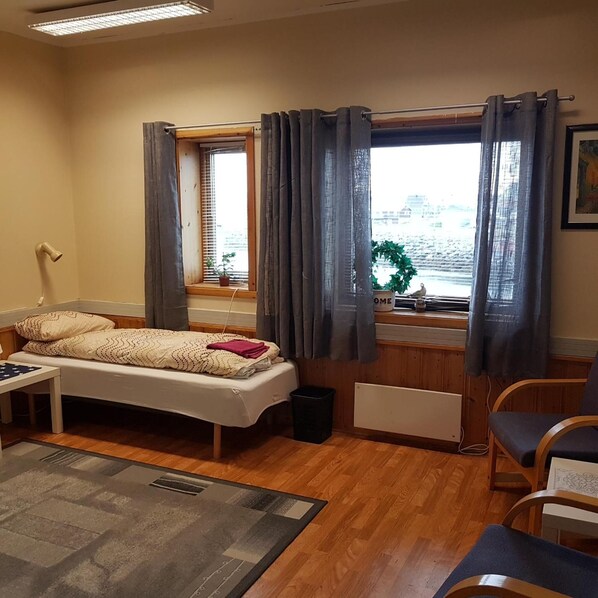 A small, cozy room with a single bed, a desk, a chair, and a window with curtains.
