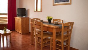 A dining area with a wooden table and chairs, a television on a wooden cabinet, and a framed picture on the wall. - Cozy 2-room apartment for 4, mountain view balcony, pets allowed. (Le Dévoluy)