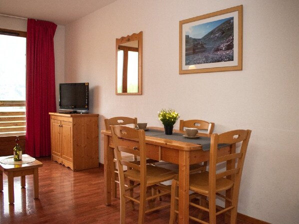 Ein Essbereich mit Holztisch und -stühlen, einem Fernseher auf einer Holzkommode und einem gerahmten Bild an der Wand.