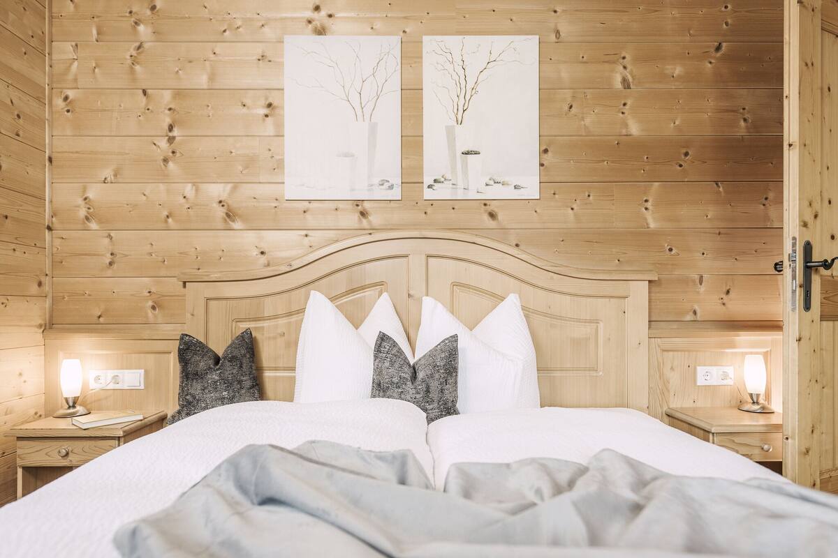 A cozy wooden cabin bedroom with a large bed, two nightstands, and two wall-mounted paintings.