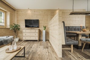 A cozy room with wooden walls, a TV mounted above a wooden dresser, a dining area with a bench, and a potted plant. - Feriendorf Joggler (Rohrberg)