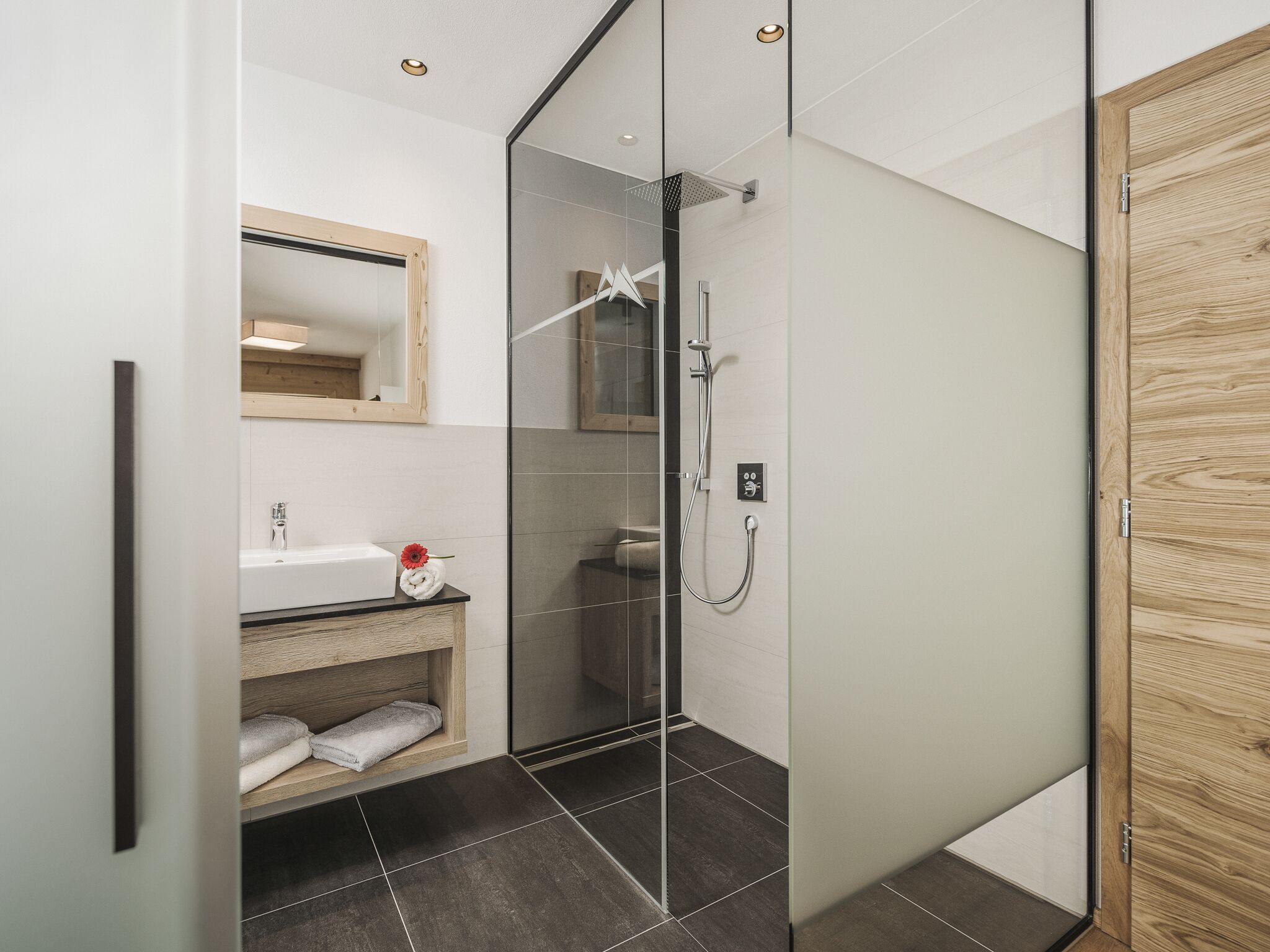 A modern bathroom with a glass shower enclosure, a wooden vanity, and a mirror.