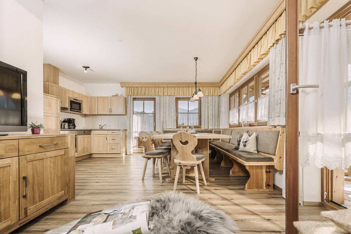A modern kitchen with wooden cabinets, a dining area with a bench, and a cozy seating area with a fur rug.