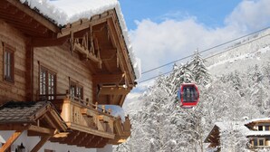 Un chalet en bois doté d’un balcon, avec un télésiège en arrière-plan et des arbres couverts de neige.