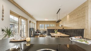 Une cuisine moderne dotée d’un îlot central, de lambris en bois et de grandes fenêtres offrant une vue sur l’extérieur.