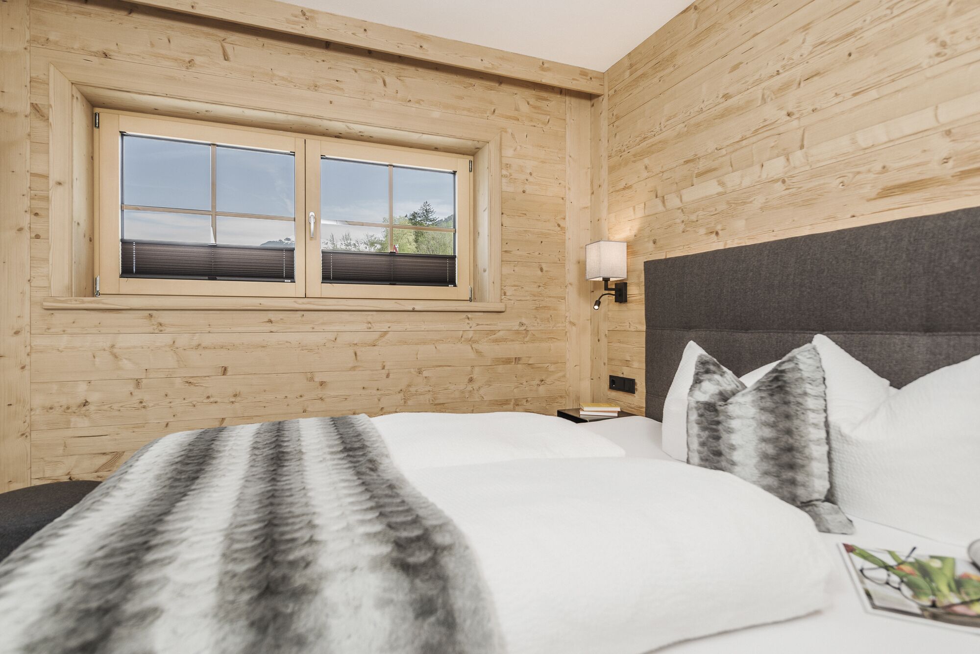 A bedroom with a wooden wall, a large bed with white bedding, and a window with blinds.