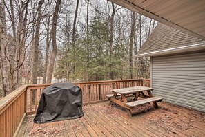 Une terrasse en bois avec une table de pique-nique et un barbecue, le tout entouré d’arbres.