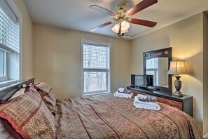 Une chambre d’hôtel équipée d’un lit, d’un ventilateur de plafond, d’une télévision, d’un bureau avec une lampe et d’une fenêtre avec des stores.