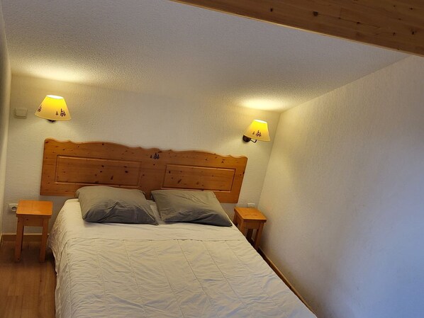 A bedroom with a wooden headboard, two bedside tables, and two wall-mounted lamps.