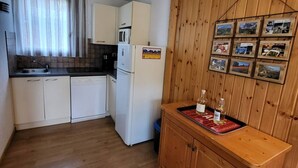 A compact kitchen with white cabinets, a microwave, and a refrigerator. There is a wooden counter with a tray holding bottles and glasses.