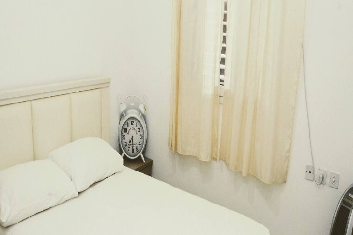 Ein Zimmer mit einem Einzelbett, einem Nachttisch mit einer Uhr und einem Heizkörper.