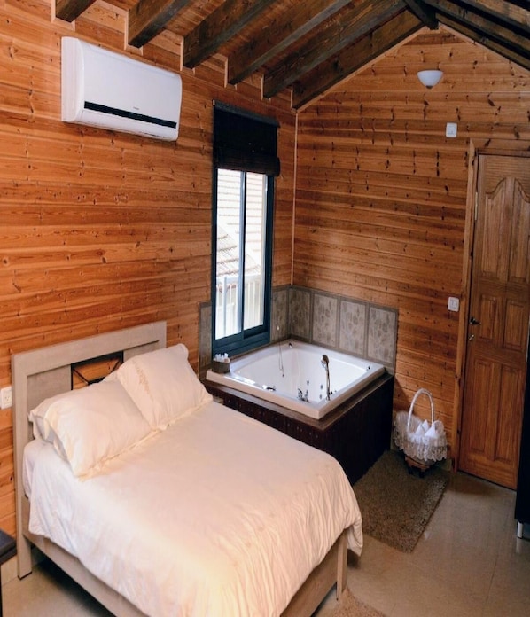 A wooden cabin bedroom with a bed, a window, a bathtub, and an air conditioning unit.