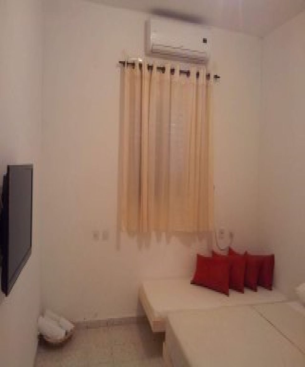 A room with a bed, a small table, a wall-mounted air conditioner, and a curtain.