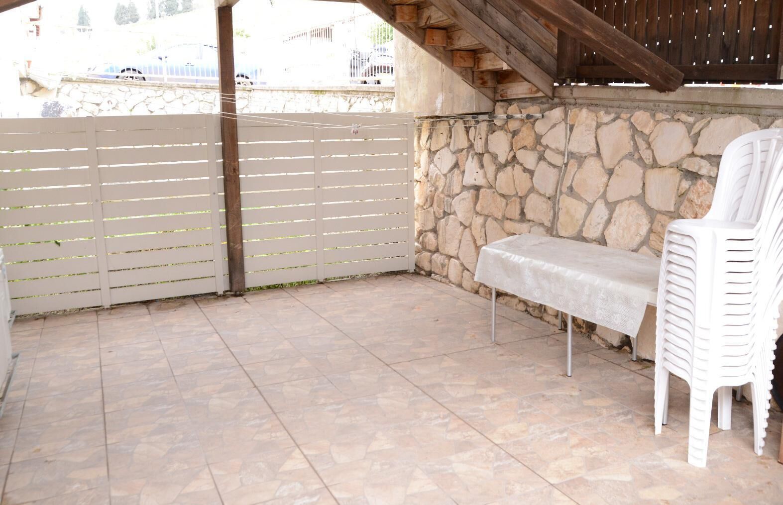 A covered patio area with stone walls, a white plastic chair, and a table with a tablecloth.