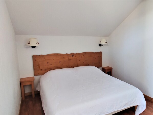 A bedroom with a wooden headboard, two bedside tables, and a white bedspread. - Duplex Chalet 6 pers, Pets allowed (Le Dévoluy)