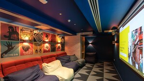 A modern lounge area with a geometric patterned floor, a red sofa with multiple cushions, and a projection screen displaying an image. - Dominick Place (Dublin)