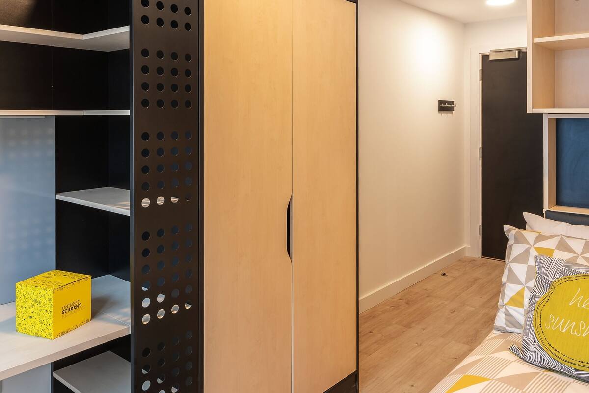 A bedroom with a wardrobe, a bed with patterned bedding, and a shelf unit.