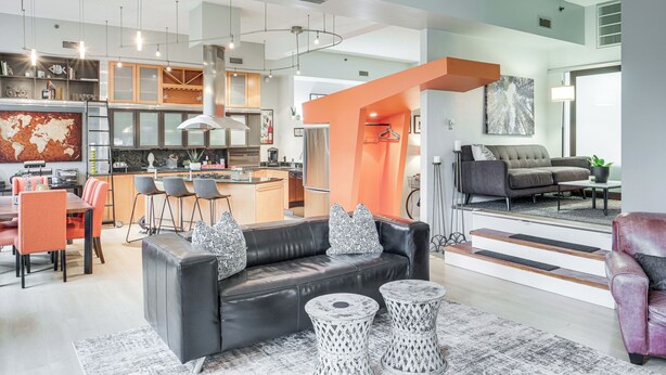 A modern living room with a black leather sofa, two round side tables, and a dining area with orange chairs. - Dtwn Cleveland Loft-Style Condo: Walk to Stadiums! (Cleveland)