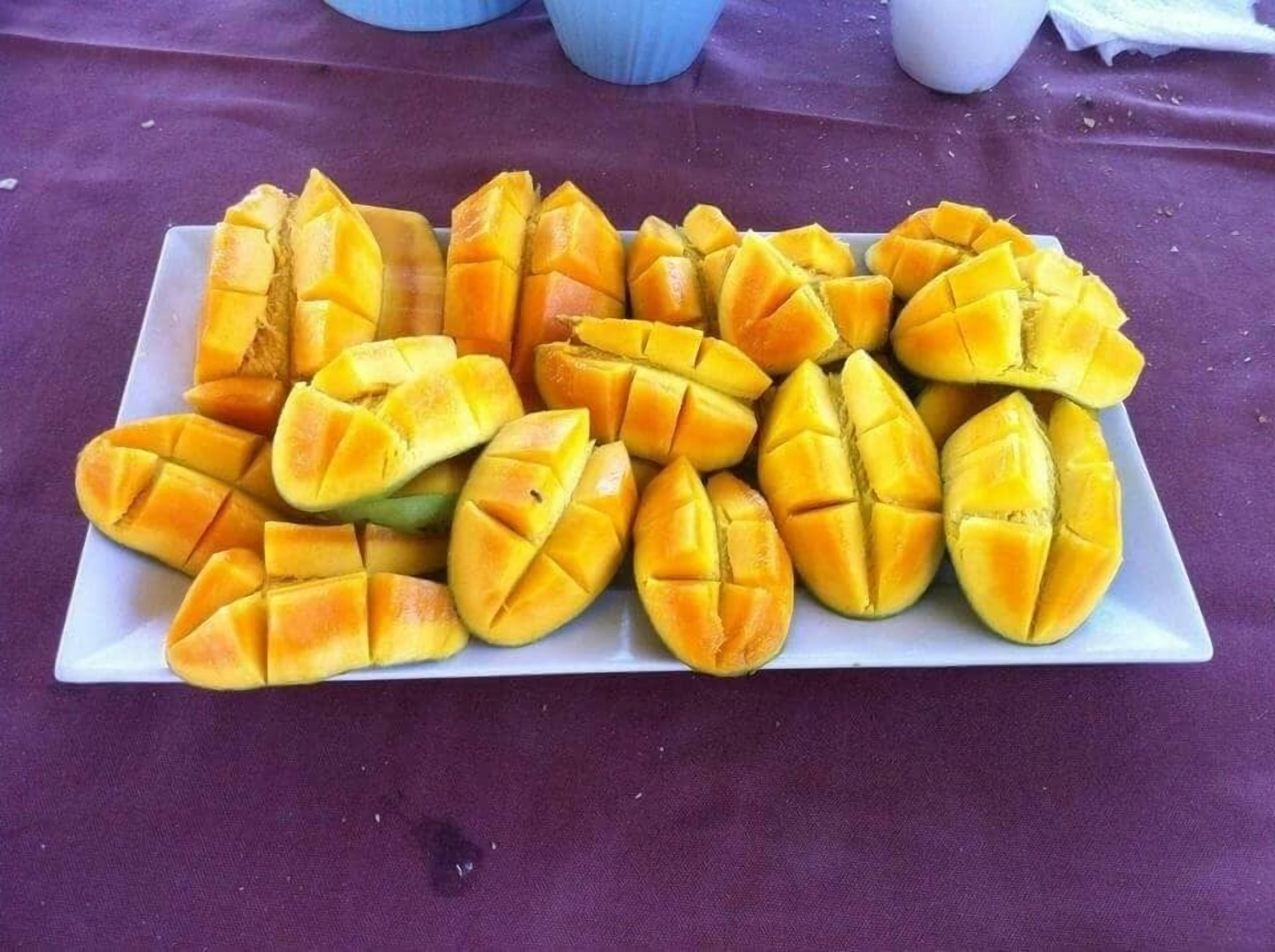 Plato blanco rectangular lleno de rebanadas de mango dispuestas cuidadosamente sobre un mantel púrpura.