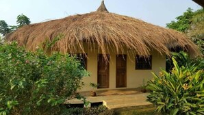 A thatched-roof hut with a single door and window, surrounded by lush greenery. - Eden Lodge Kribi (Kribi)