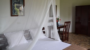 A bedroom with a bed covered by a white canopy, a wooden headboard, a desk with a chair, and a wardrobe. - Eden Lodge Kribi (Kribi)