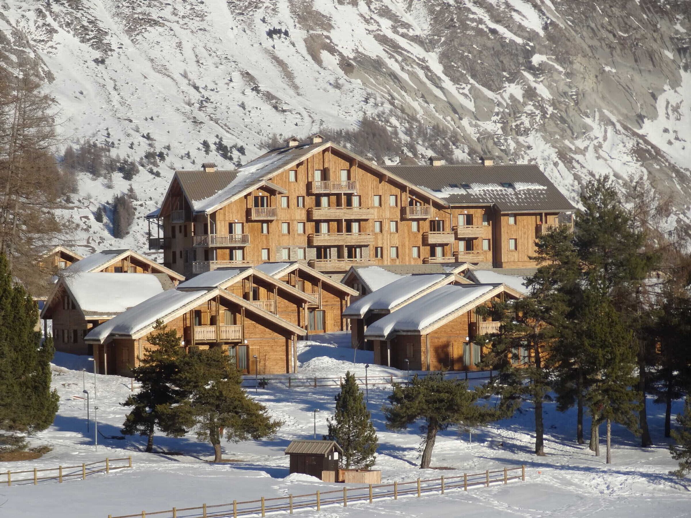 A large wooden lodge with multiple balconies and a mountain backdrop.