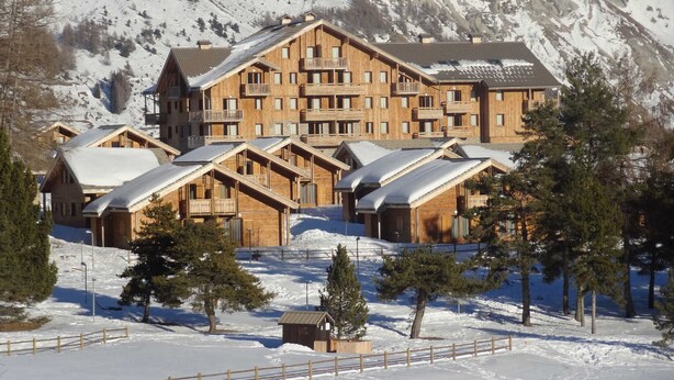 Un gran refugio de madera con varios balcones y un paisaje de montaña al fondo.