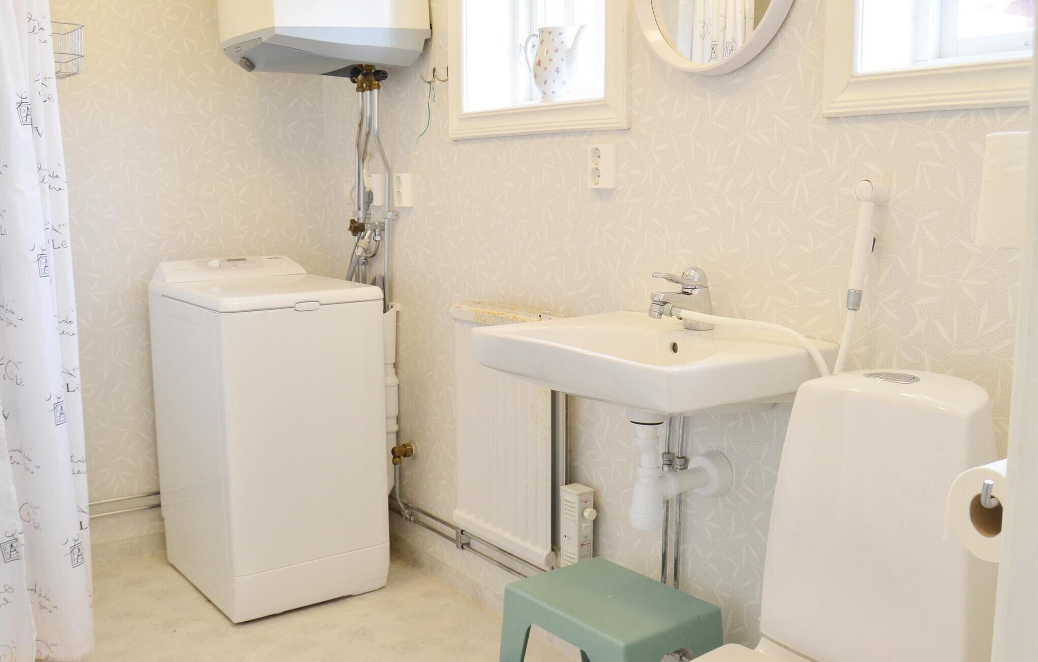 A bathroom with a washing machine, a sink, a toilet, and a small stool.