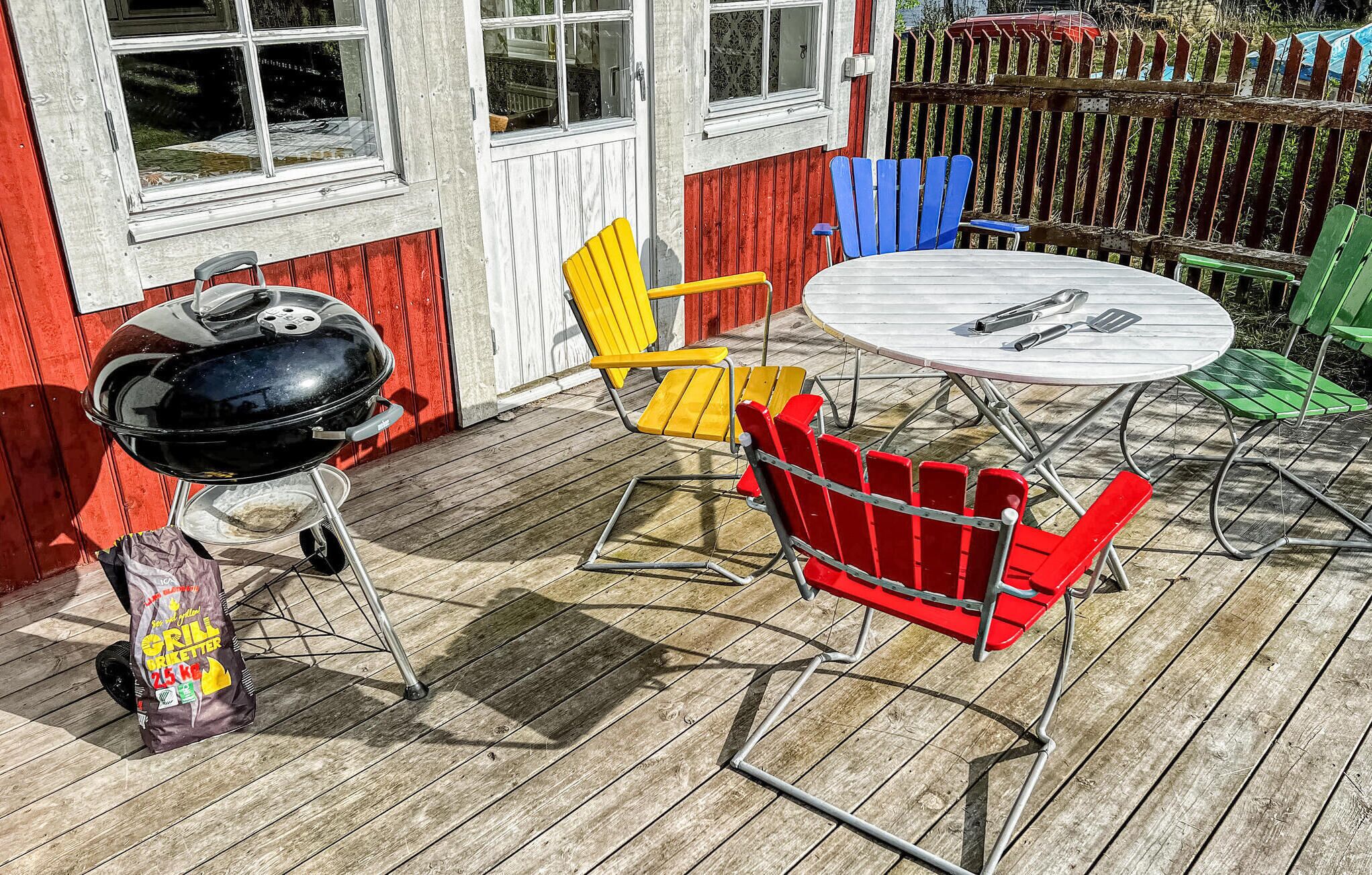 Une terrasse en bois avec un barbecue, un coin salon extérieur avec des chaises colorées et une table ronde.