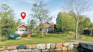 A lakeside property with a stone wall, a wooden dock, and two red houses with white trim. - Lovely home in Gräddö with sauna (Gräddö)