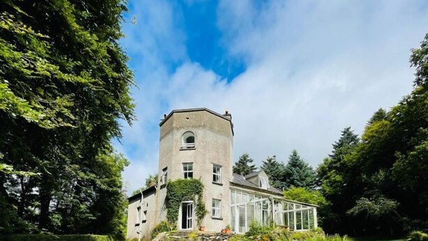 A large, historic building with a tower, surrounded by lush green grass and trees.