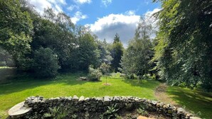 A stone pathway leading through a lush garden with a stone wall and a bench.