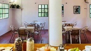 Un área de comedor con mesas y sillas, una columna central, y diversos alimentos sobre las mesas.