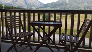 Un balcón con dos sillas de madera y una mesa, con vistas a un paisaje montañoso.