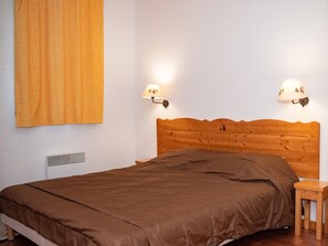 A bedroom with a wooden headboard, a brown bedspread, two wall-mounted lamps, and a small wooden nightstand. - Apartment 8 pers, ski locker and balcony (Le Dévoluy)