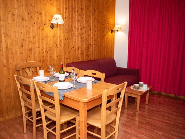A dining area with wooden walls, a wooden table set for four, and a red curtain in the background. - Apartment 8 pers, ski locker and balcony (Le Dévoluy)