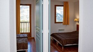 Un dormitorio con cama, ventana con cortinas, mesita de noche y vistas al exterior.