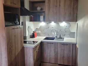 Une cuisine compacte avec des meubles en bois, un four à micro-ondes, une bouilloire et un crédence moderne en carreaux.