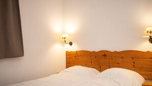 A neatly made bed with white linens in a room with a wooden headboard and two wall-mounted lamps. - 3-Room Apartment, 6 People, Pets Allowed, Balcony (Le Dévoluy)